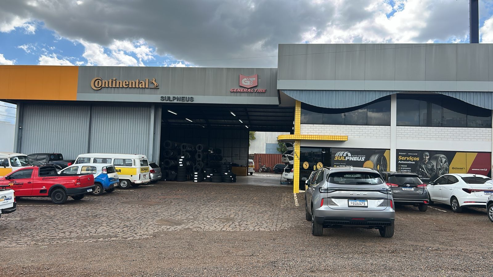 Um homem de macacão amarelo segura um pneu na frente de um carro.