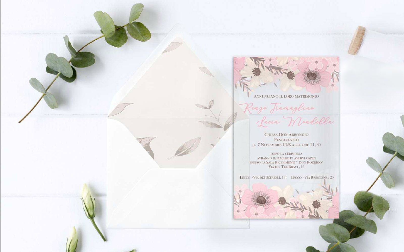 Un invito di nozze è appoggiato su un tavolo bianco accanto a una busta bianca.