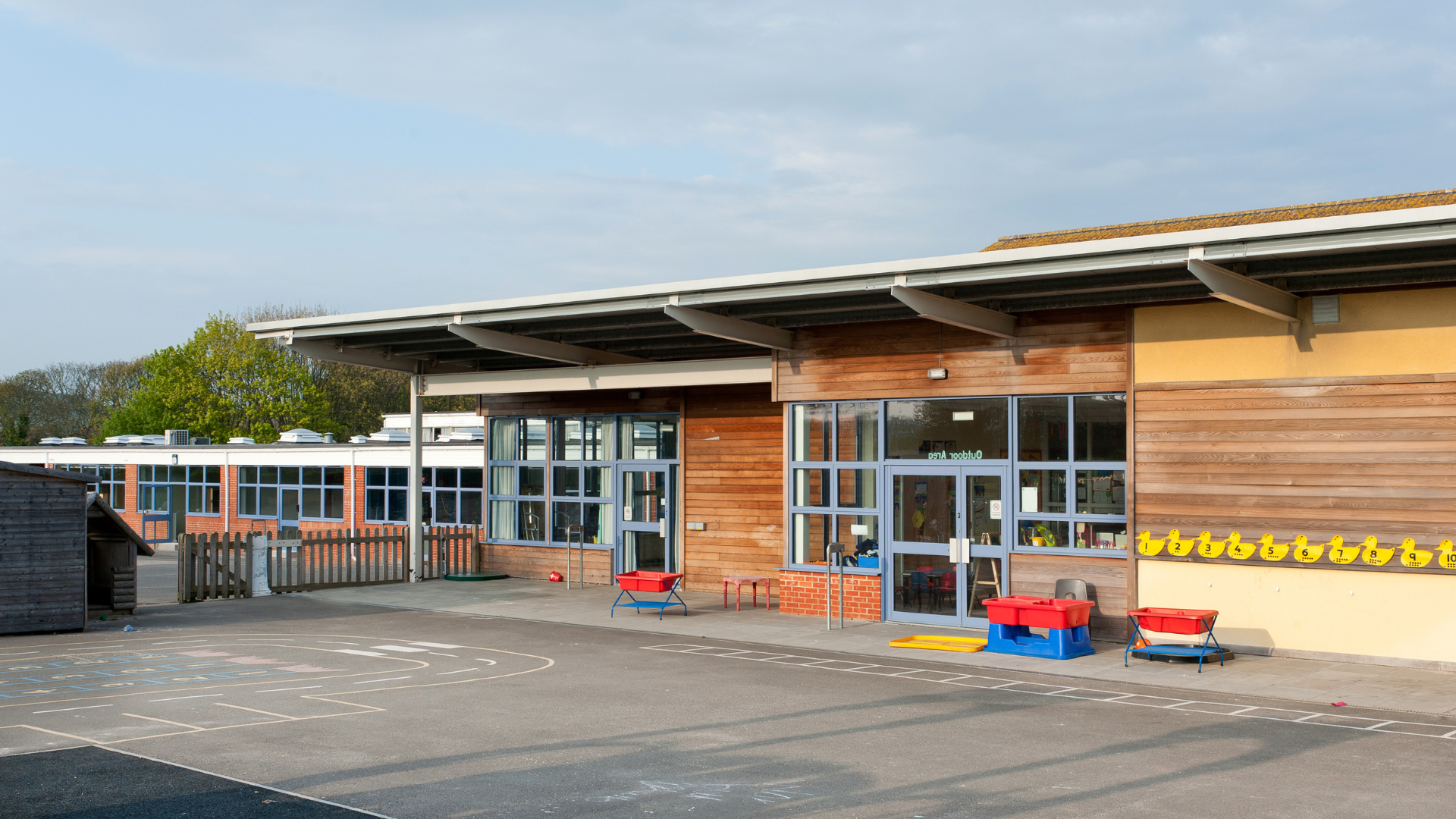 School building exterior with glass doors, wooden siding, and a playground area.