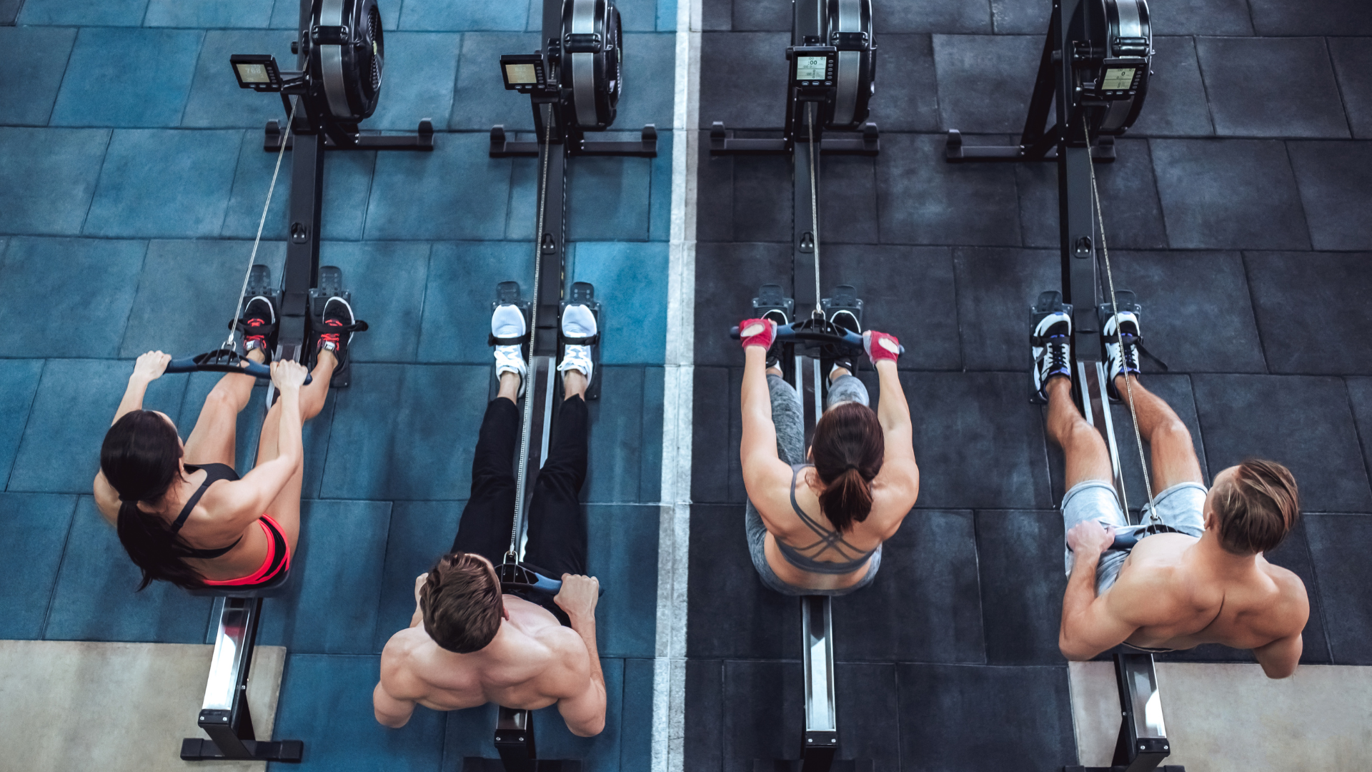 Four people rowing on exercise machines in a gym.