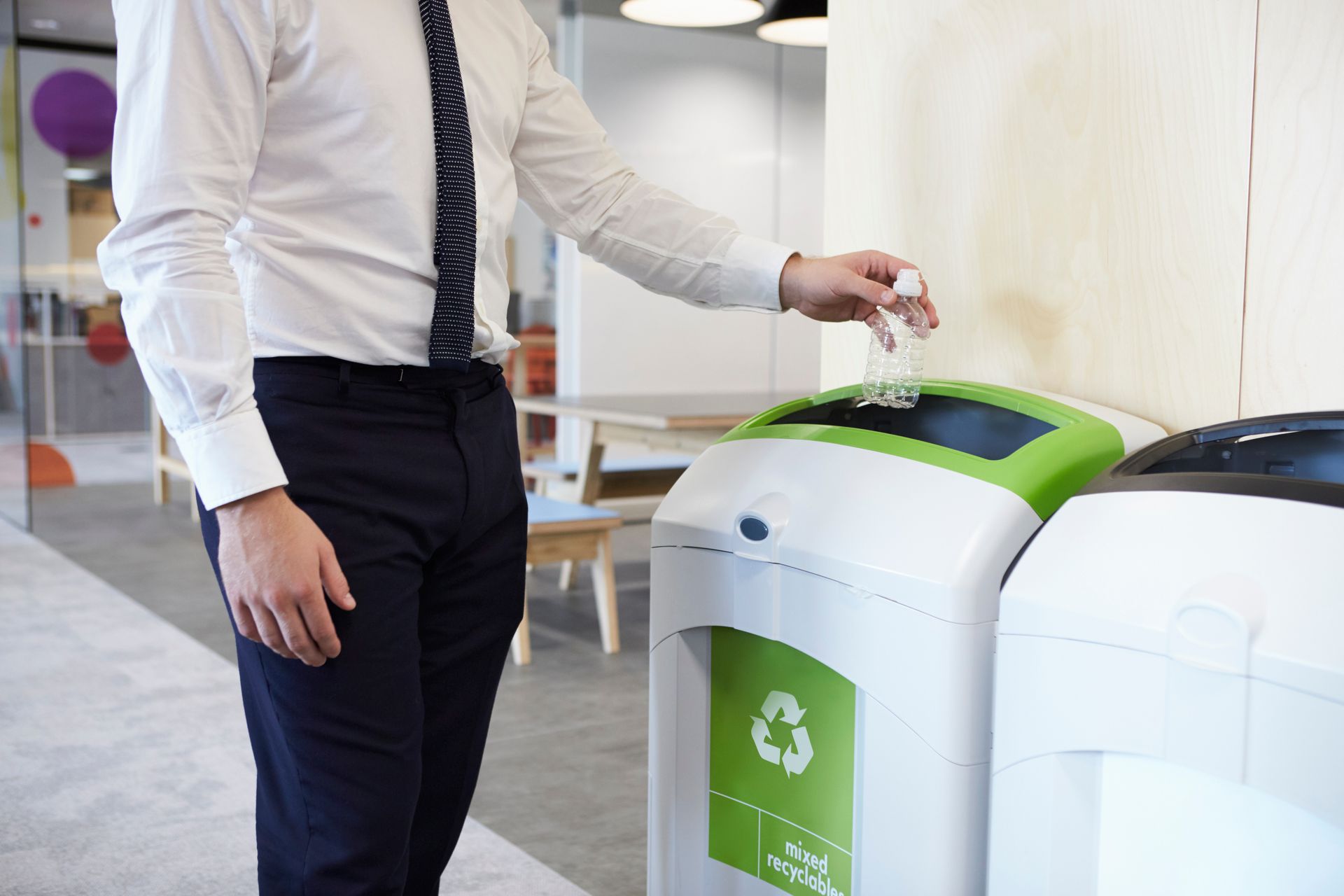 A man is throwing a plastic bottle into a recycling bin.