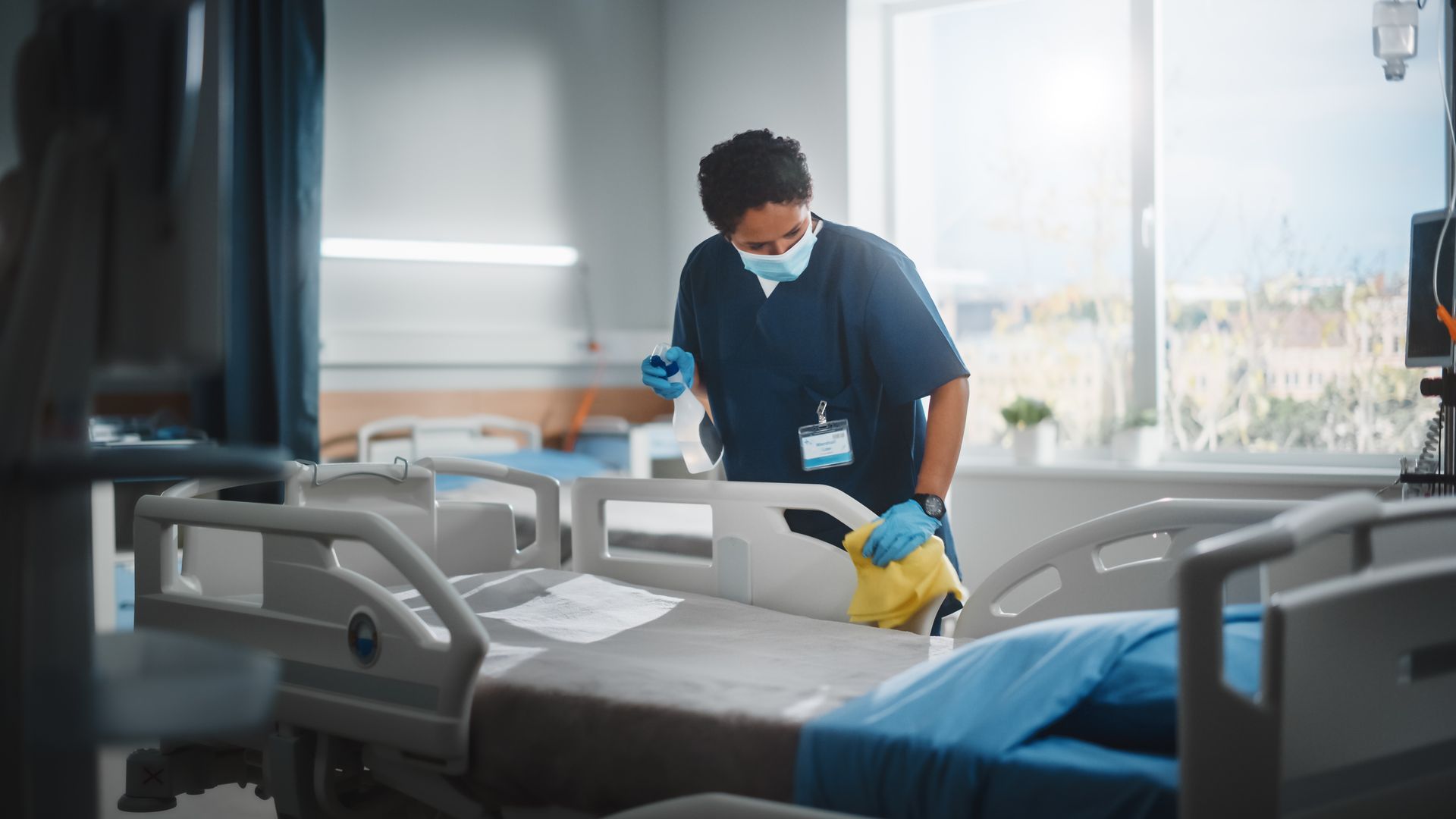 A professional cleaner is cleaning a hospital bed in a hospital room.