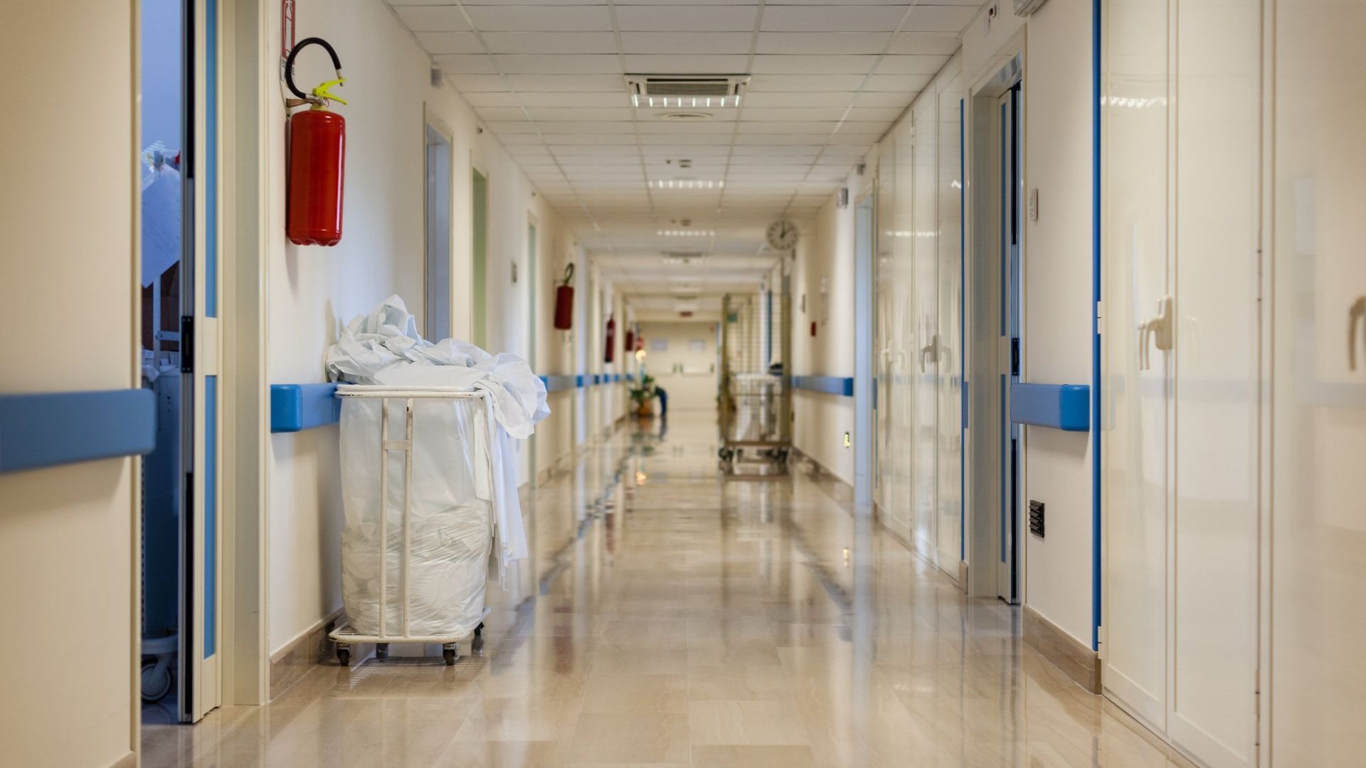 A well cleaned hospital hallway with a trash can in the middle.