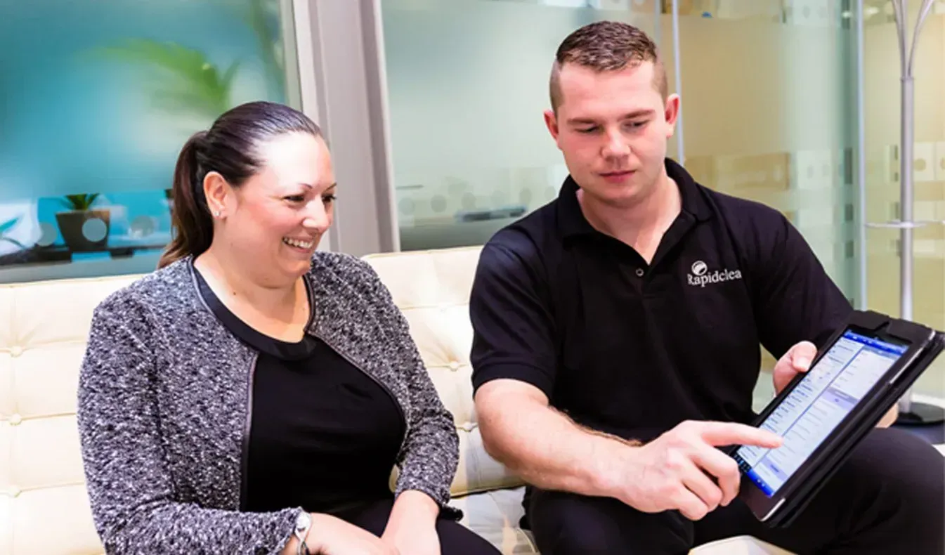 A man and a woman are sitting on a sofa looking at a professional cleaning contract.