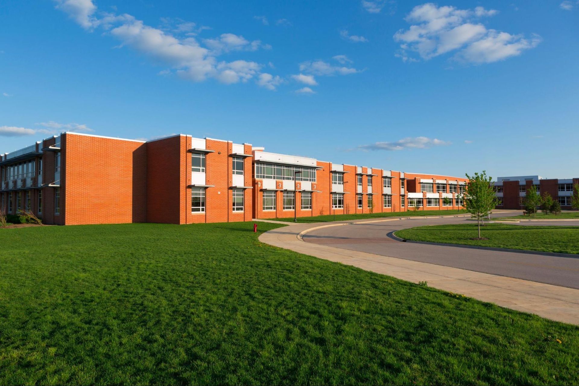 A large brick building with a lot of windows is sitting on top of a lush green field.