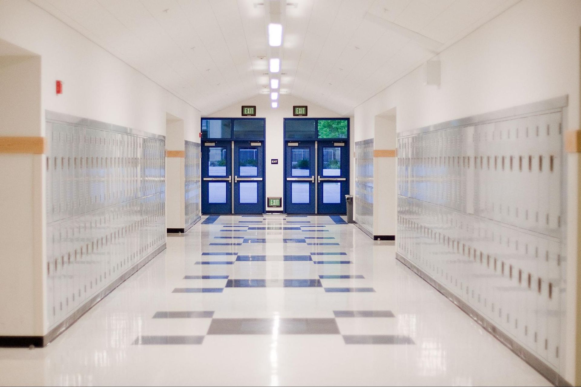 An empty school hallway with lockers and blue doors.