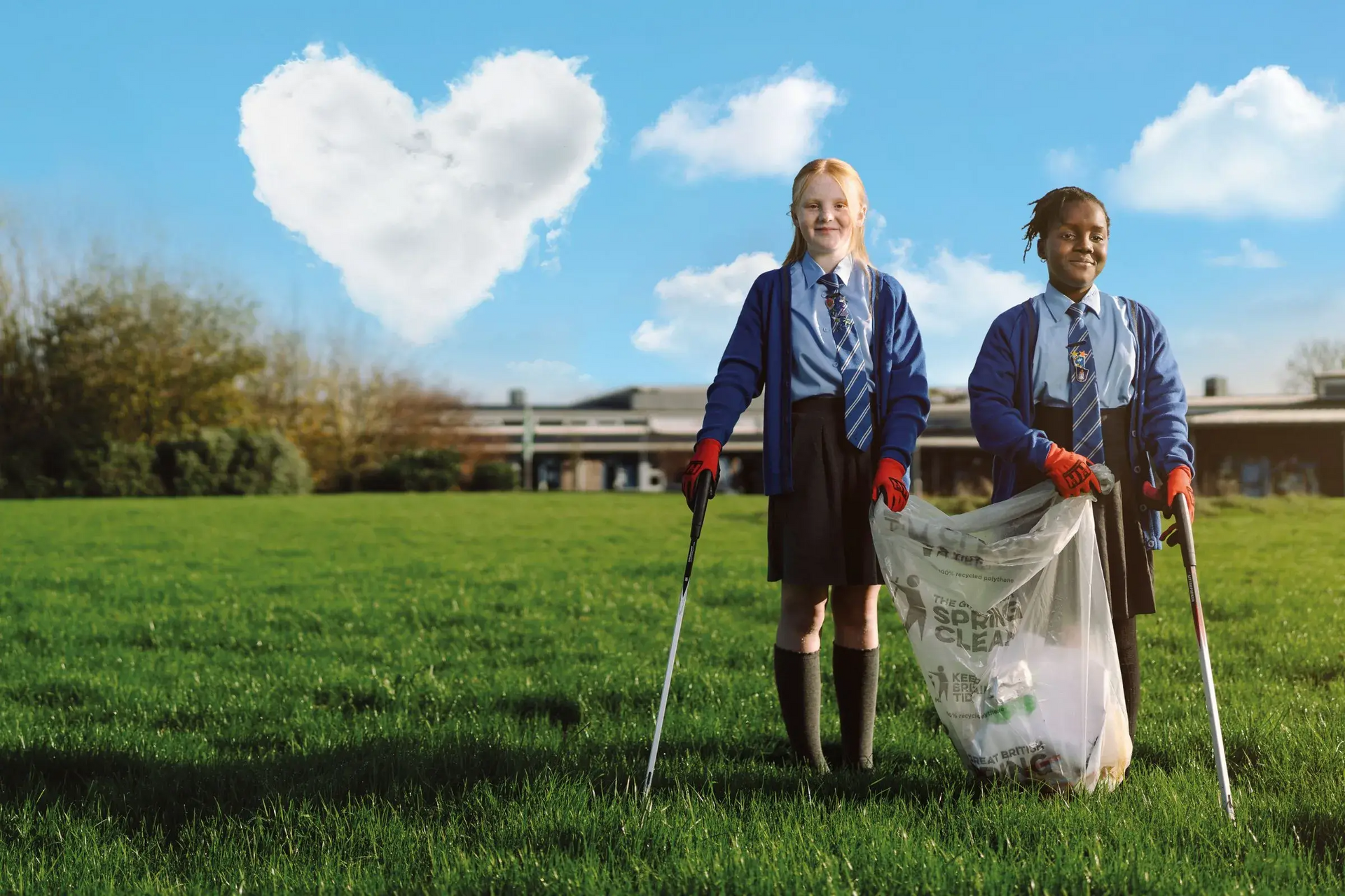Two girls in school uniform are litter picking in a school field, a heart-shaped cloud is in the sky