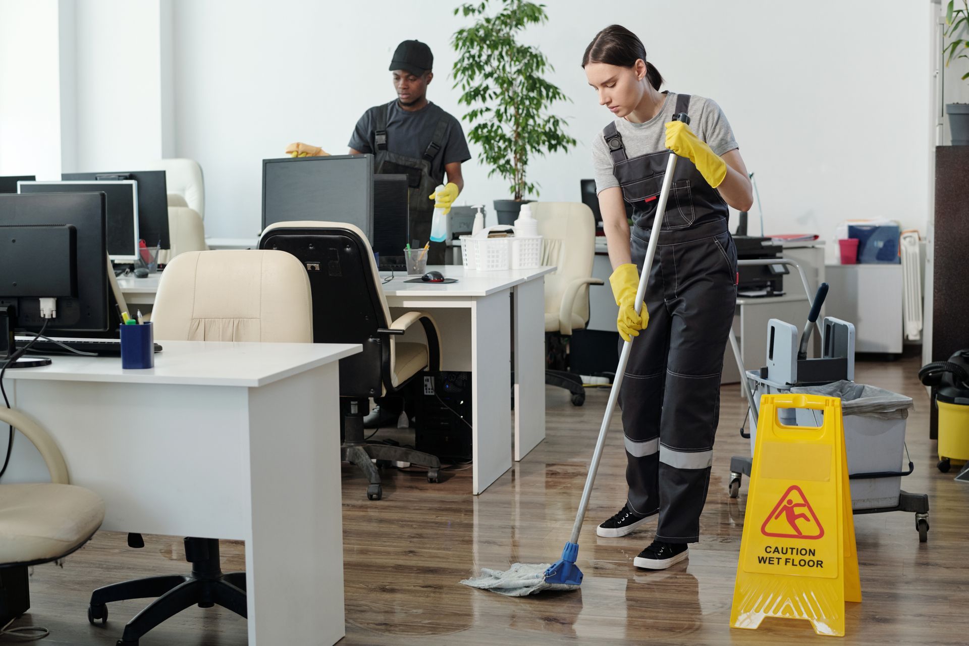 Two office cleaners are cleaning an office with a mop and cloth