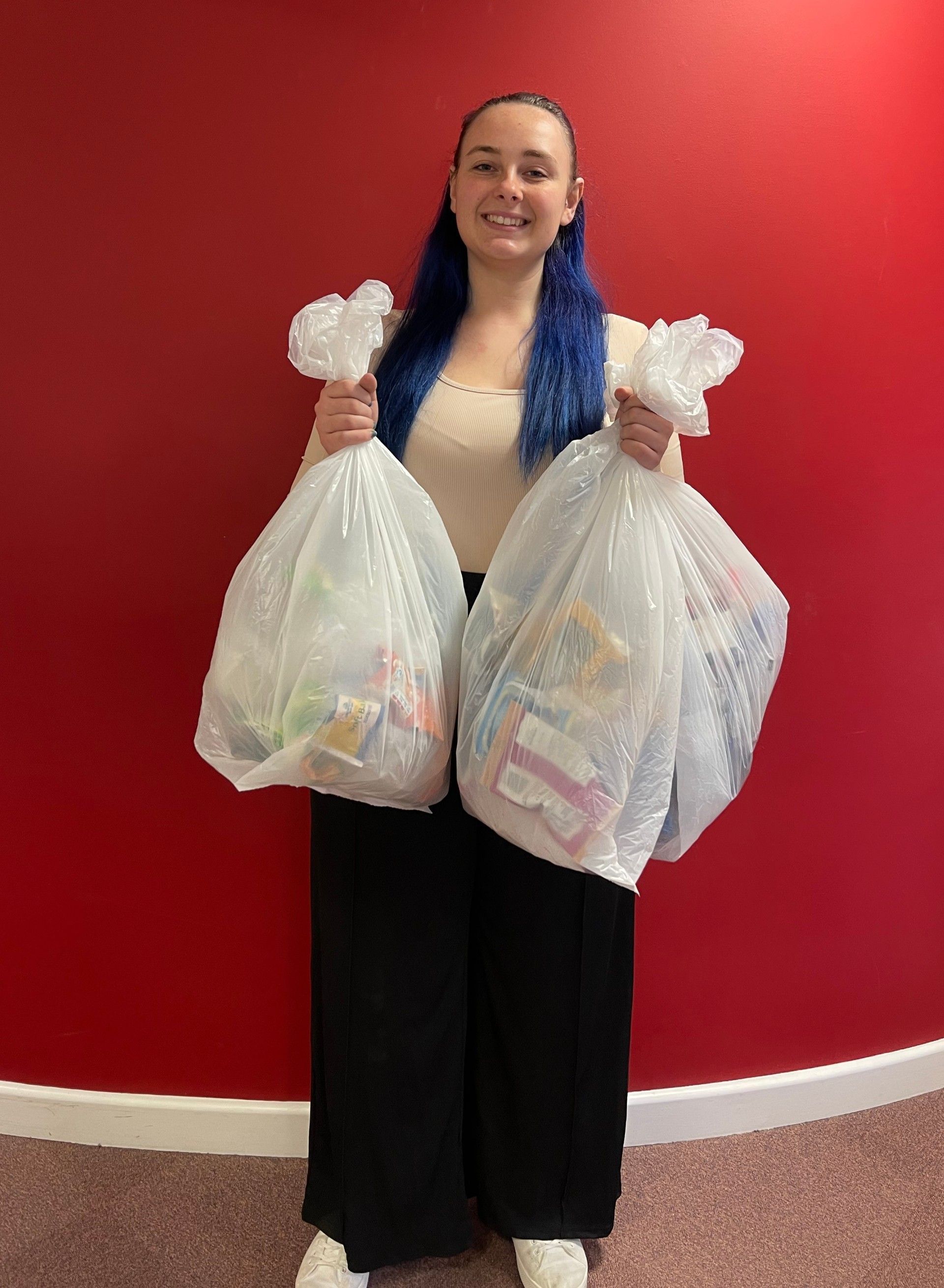 A woman is holding two bags of clothes in front of a red wall.