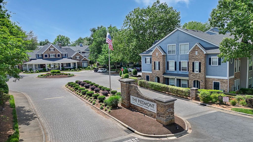 Exterior view of The Piedmont apartment community with entry sign, landscaping, and an American flag.