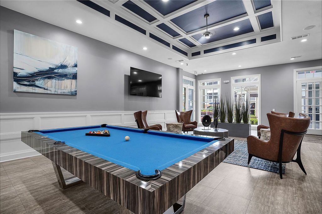 Indoor amenity room with a blue pool table, modern seating, a wall-mounted TV, and large windows.