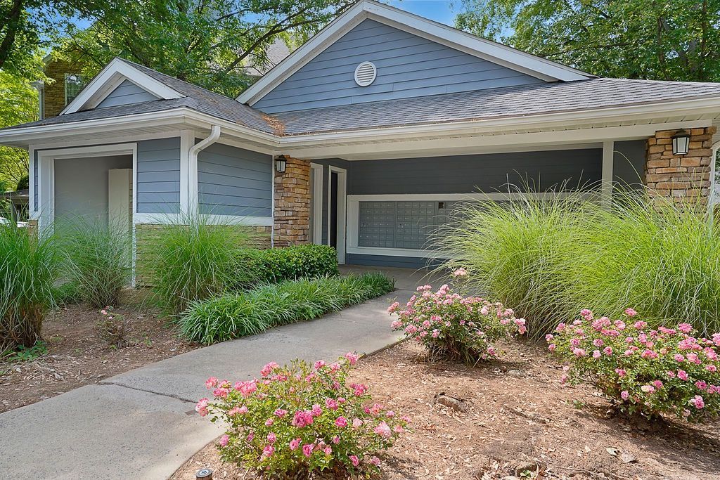 Exterior view of a blue townhouse-style apartment building with a landscaped walkway and pink rose bushes.