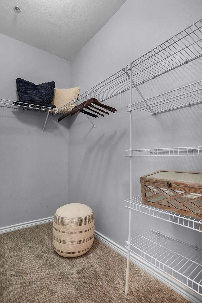 Walk-in closet with white wire shelving, clothing rods, and a round woven ottoman.