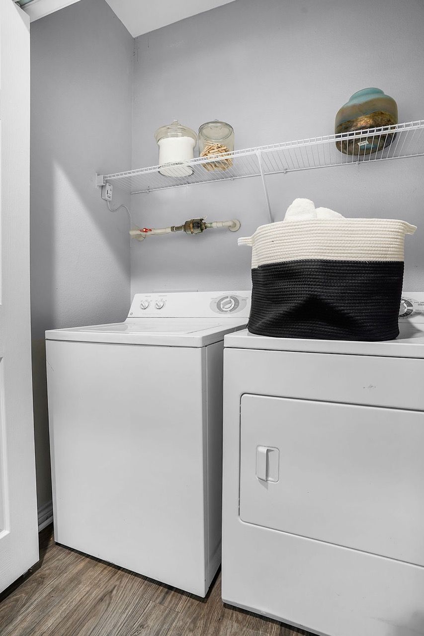 Laundry room with white washer and dryer side by side and a wire shelf above.