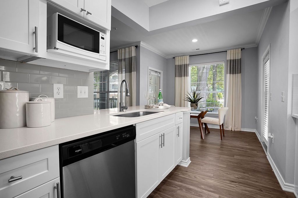 White kitchen with stainless steel appliances and a small dining nook by a window.