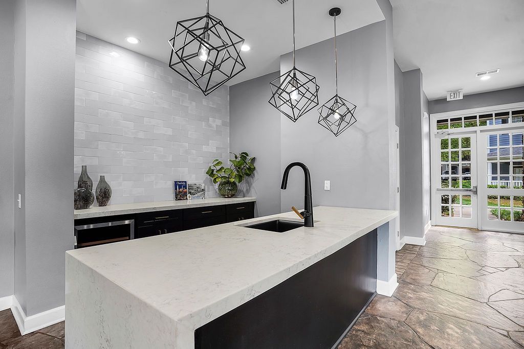 Modern community kitchen with a white island, black faucet, pendant lights, and glass doors at the entrance.