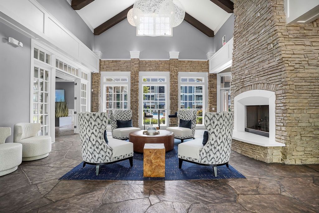 Lobby seating area with four patterned chairs around a round coffee table near a stone fireplace.
