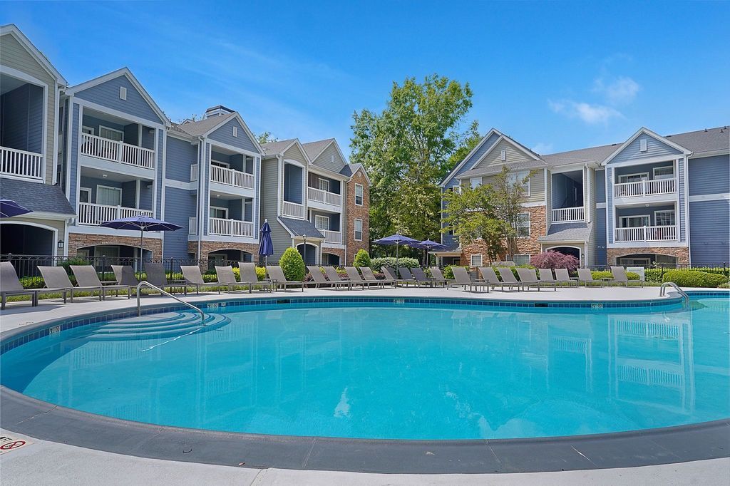 Outdoor pool area at a modern apartment community with lounge chairs and blue building facades.