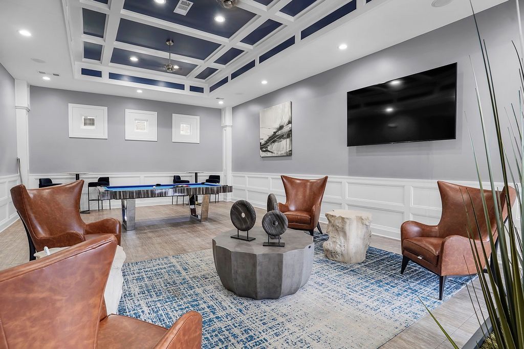 Modern resident lounge with a pool table, brown leather chairs, rug, and a wall-mounted TV.