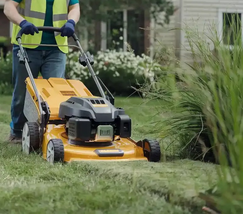 A man is using a lawn mower to cut the grass in a garden.