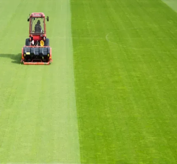 A man wearing a yellow hard hat is mowing his lawn