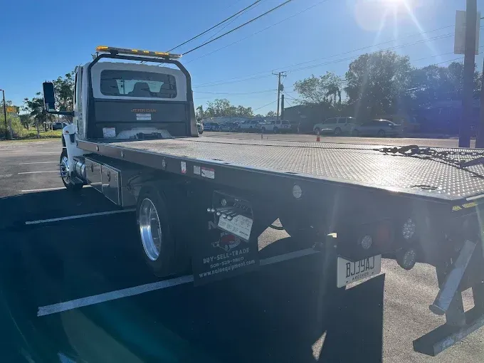 White flatbed tow truck on asphalt in sunlight.