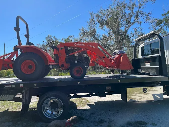 Orange Kubota tractor with a front loader, on a flatbed truck, outdoors.