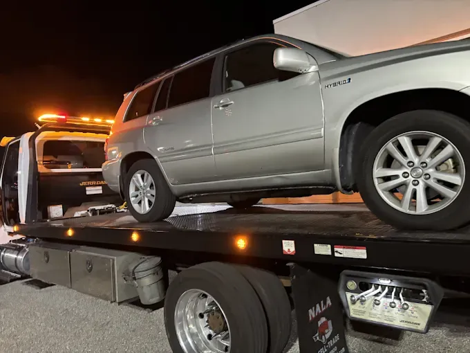 Silver Toyota SUV being towed on a flatbed tow truck at night.