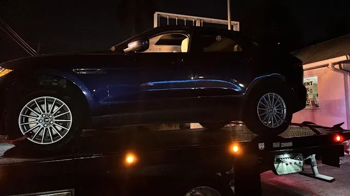 Blue SUV being towed on a flatbed tow truck at night.