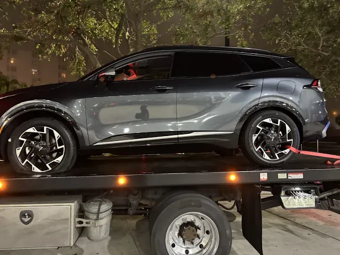 Gray Kia SUV on a tow truck, nighttime scene.