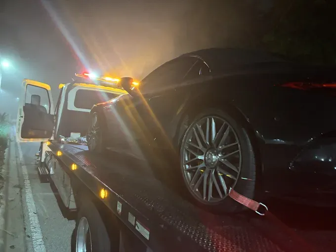Black car on a tow truck at night, with flashing lights.