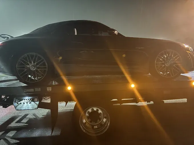 Black Mercedes-AMG GT S on a tow truck, lit by orange lights in the night.