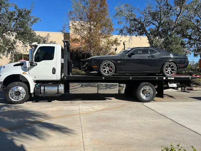 A black Dodge Challenger on a white flatbed tow truck on a sunny day.