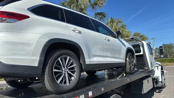 White SUV being towed by a tow truck on a sunny day.