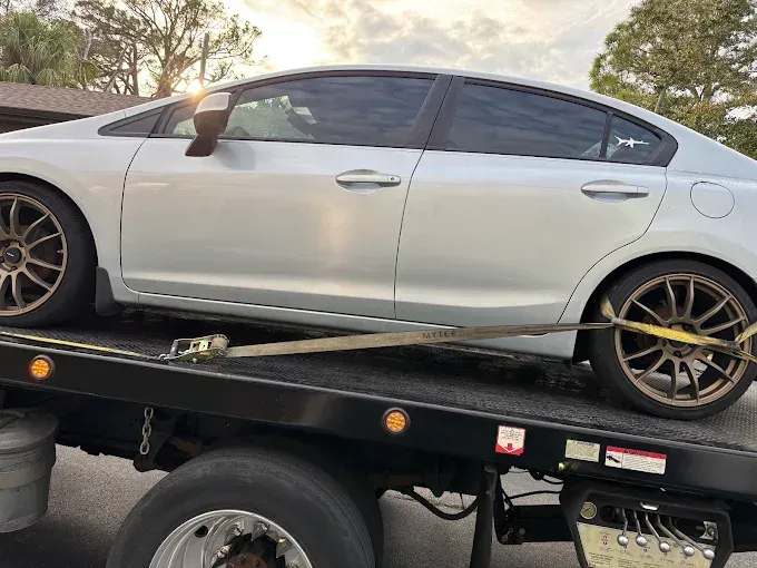 Silver sedan car being towed on a flatbed tow truck.