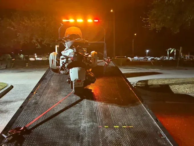 Motorcycle on a tow truck at night. Orange and red lights are on.