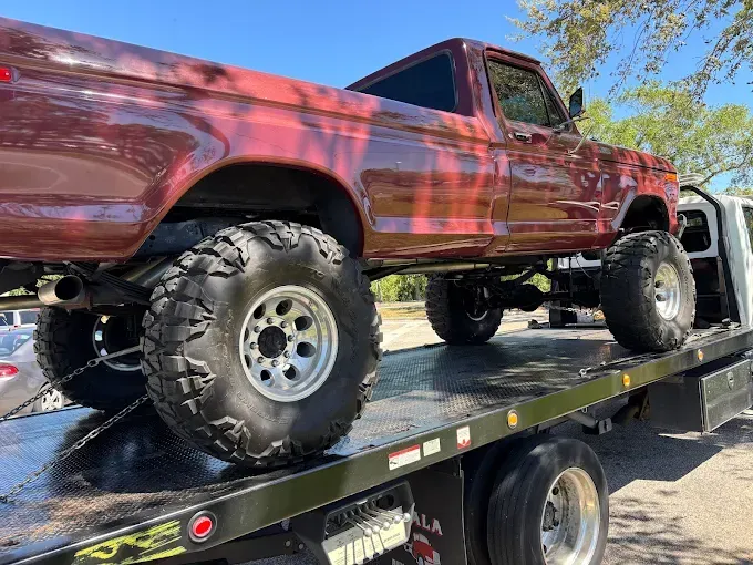 Red lifted pickup truck on a tow truck, sunlight reflecting off the paint.
