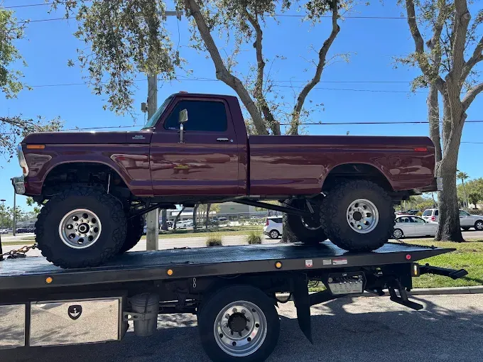 Maroon lifted pickup truck on a flatbed tow truck outdoors on a sunny day.