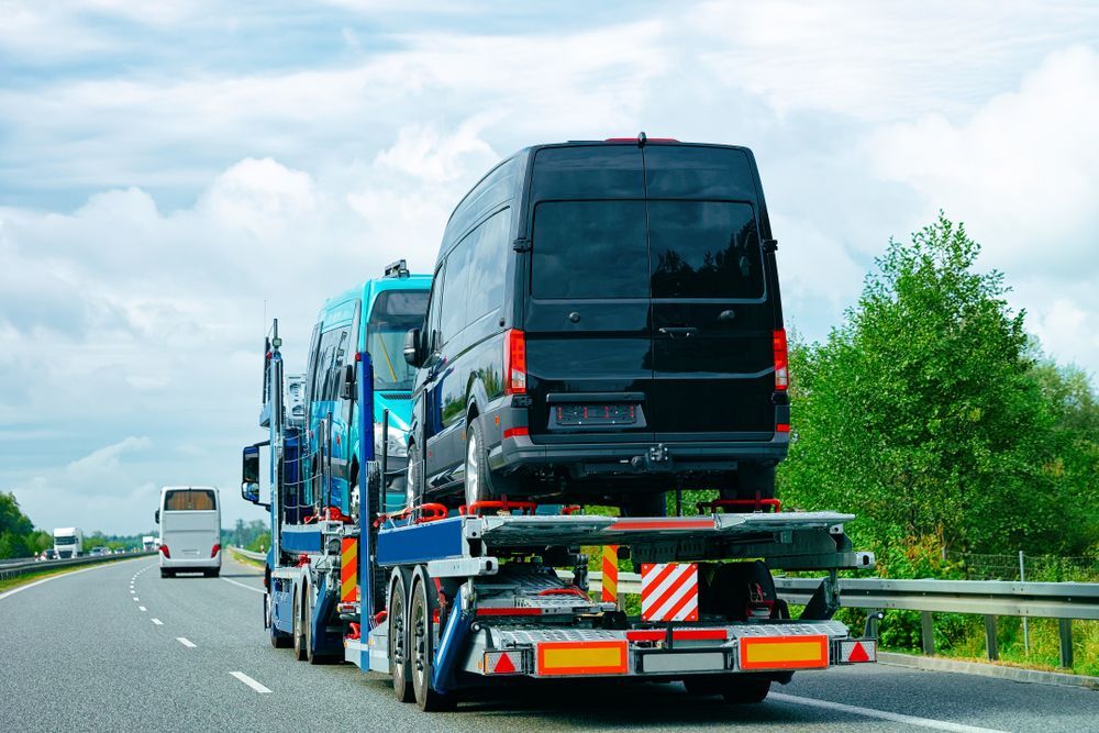 A car carrier truck transporting several new vans on a highway under a cloudy sky.