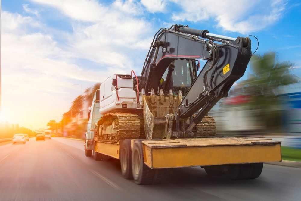 Excavator on a flatbed trailer traveling on a sunny road.