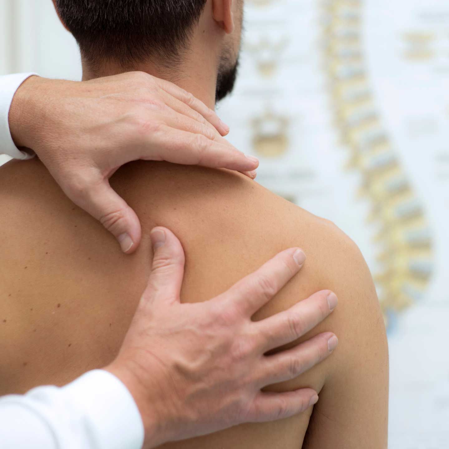 Hands of a healthcare professional examining a person's shoulder, with a spine chart in the background.