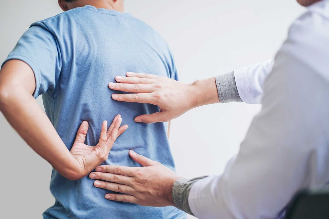 Doctor examining patient's back, palpating the lower back area. Doctor examining patient's back, palpating the lower back area.