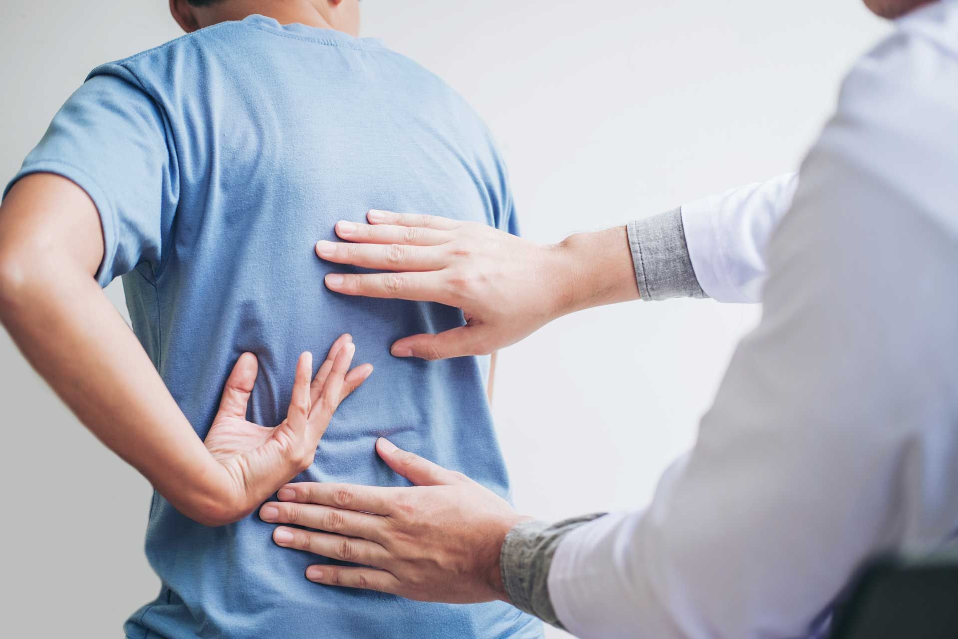 Doctor examining a patient's lower back; hands on back; blue shirt, white coat.