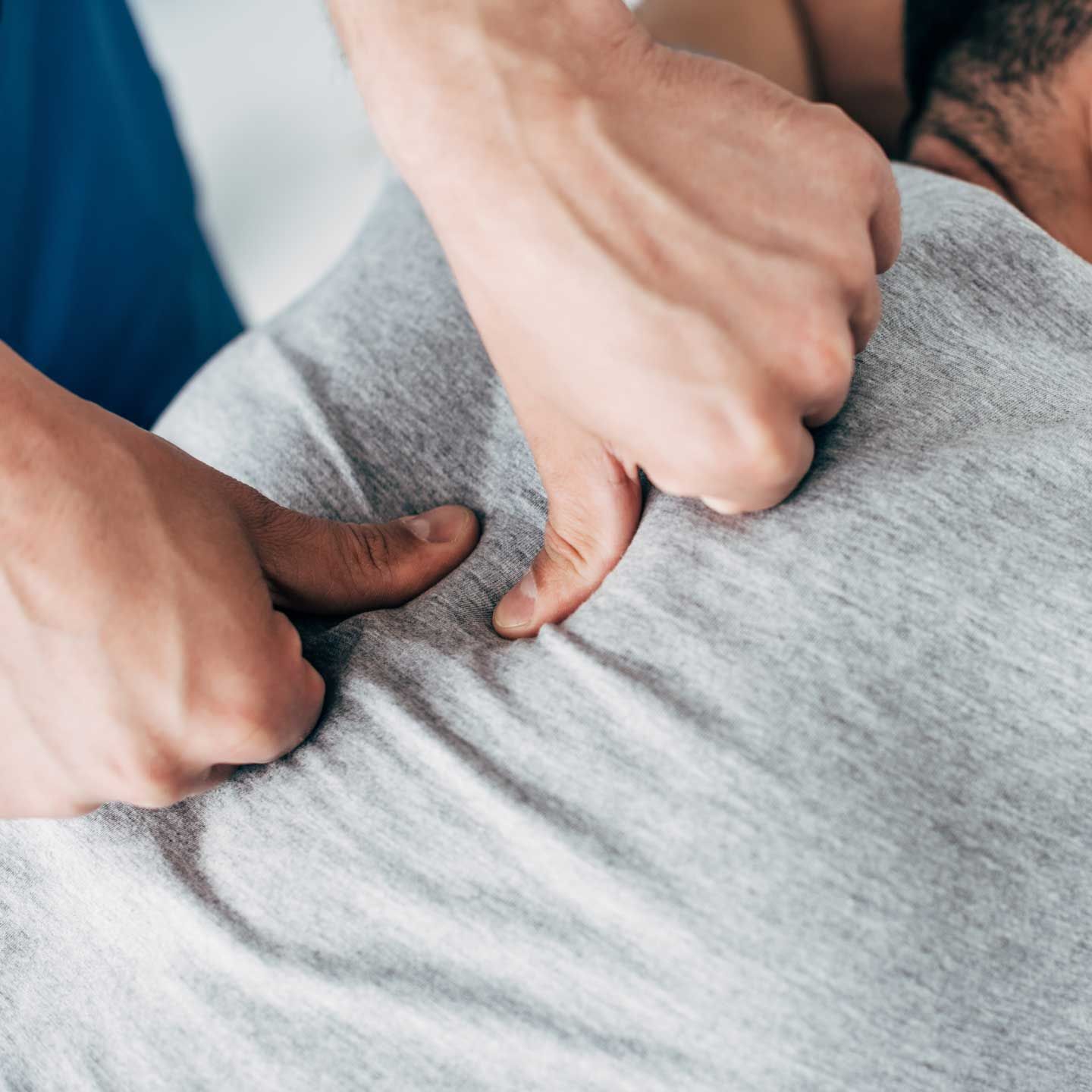 Hands massaging the back of a person wearing a gray shirt, likely in a medical setting.