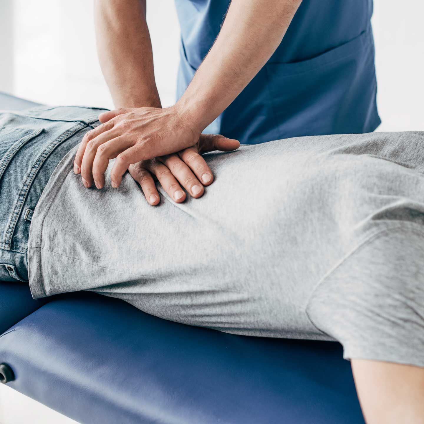 Person receiving chiropractic adjustment on a blue examination table. Chiropractor in blue scrubs with hands on patient's back.
