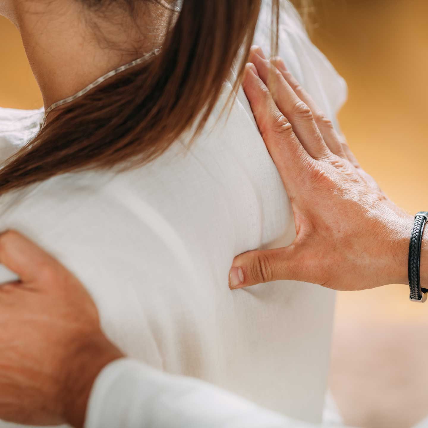 Person's back and shoulder touched by two hands, possibly providing comfort or support.
