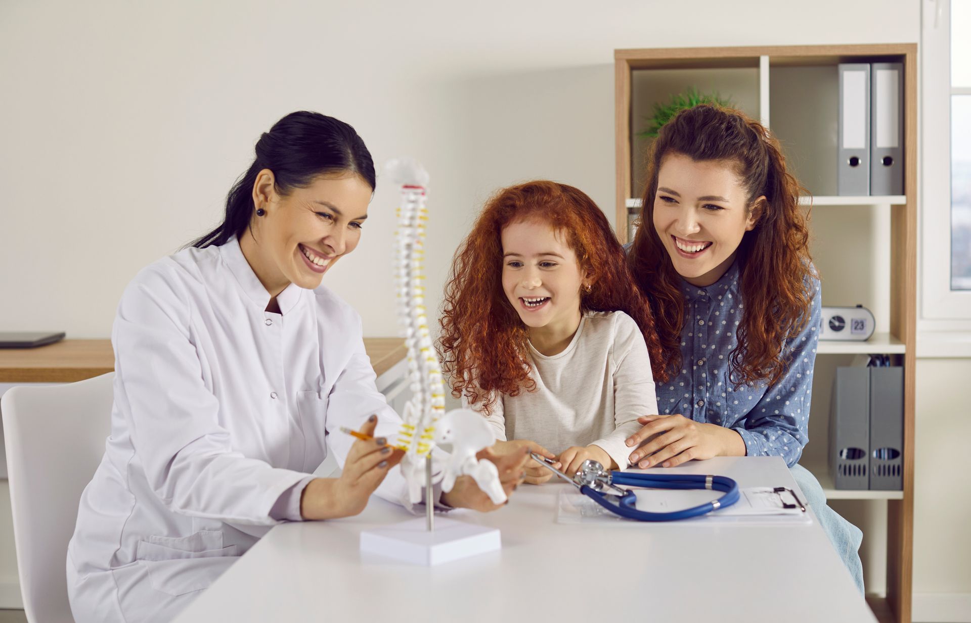 Healthcare professional explaining a spine model to a child and accompanying adult.