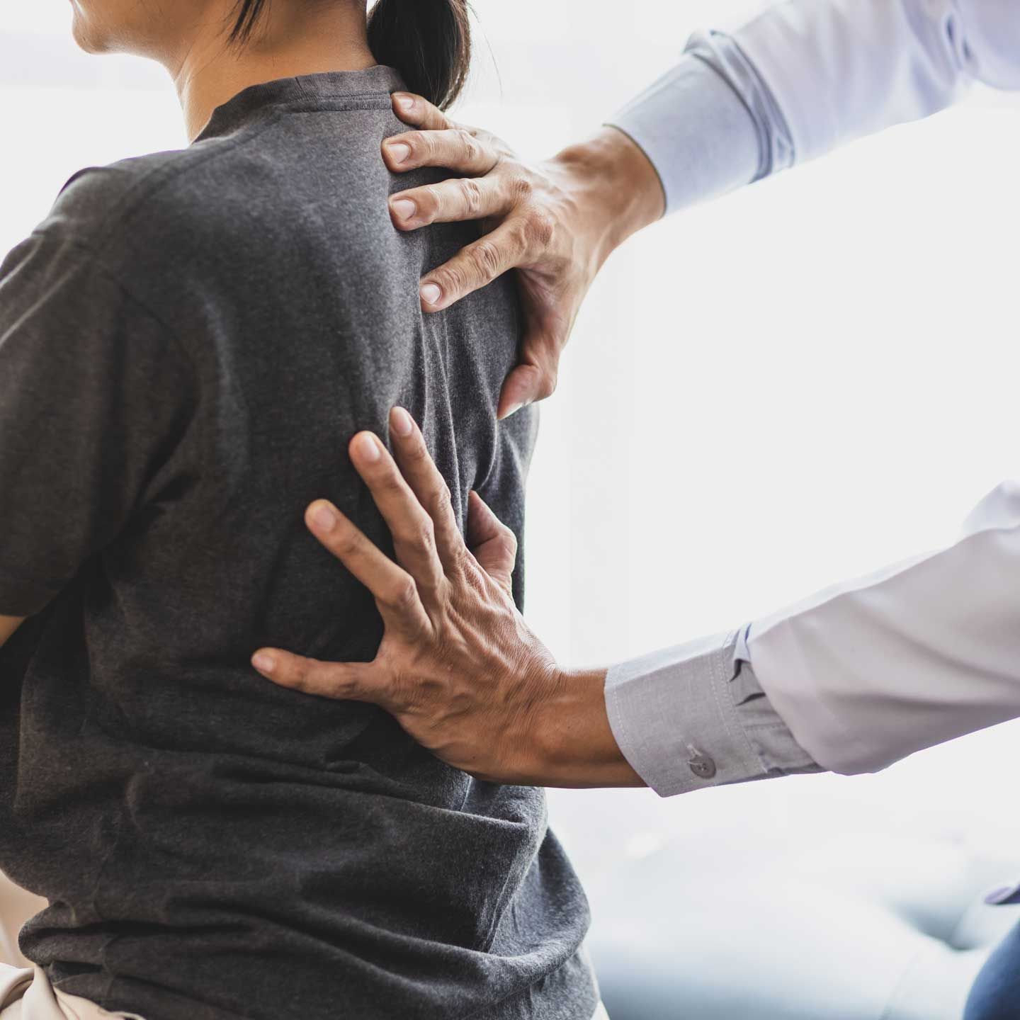 Person's back being examined by a doctor. Doctor's hands on back; indoors.