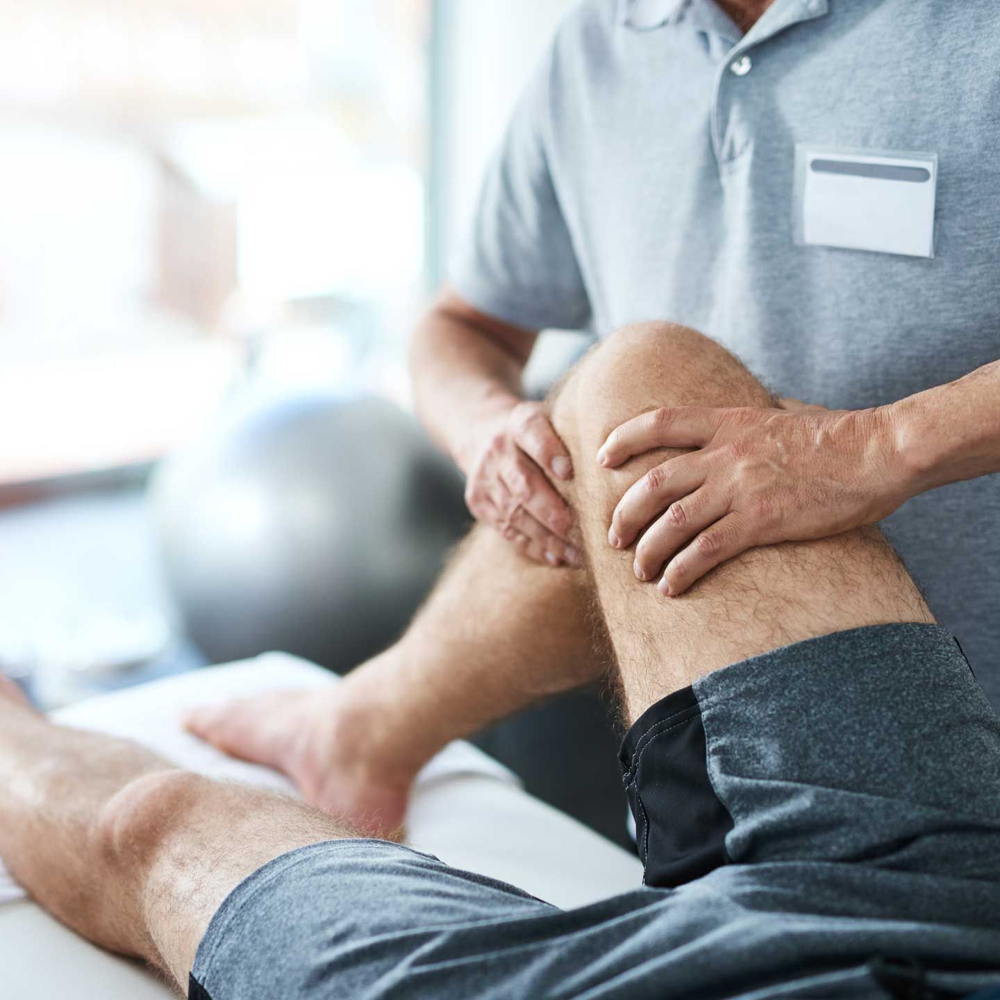 Physical therapist examining patient's knee in a clinic setting.