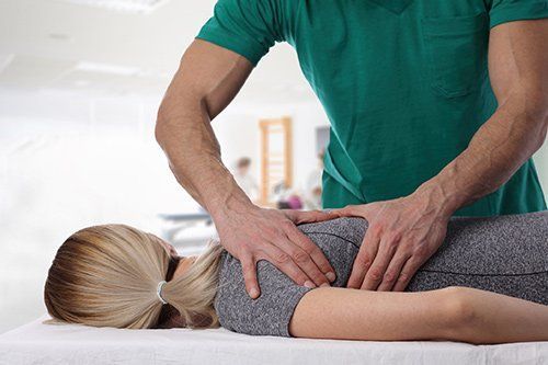 Therapist in green shirt giving back massage to person lying face down on a table.